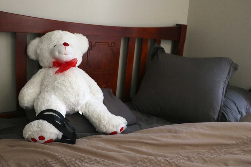 A white teddy bear on a bed.