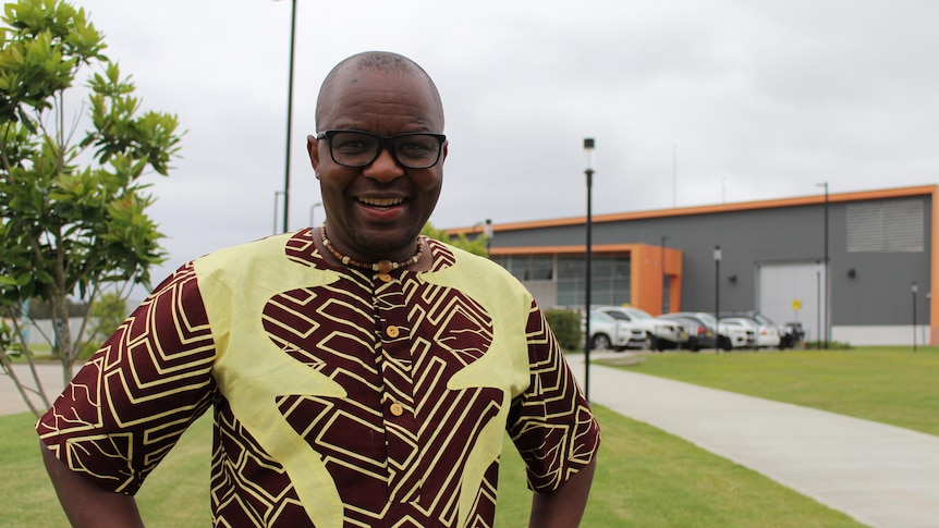 Allan Chidziva wears a yellow and brown African shirt and smiles outside at the prison.