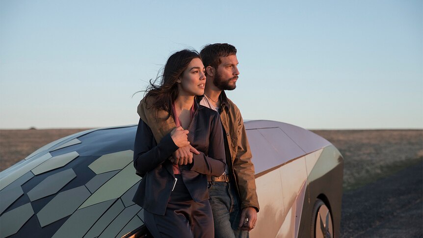Still image of Melanie Vallejo and Logan Marshall-Green leaning on a futuristic vehicle as the sun sets in 2018 film Upgrade.