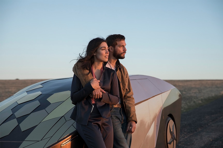 Still image of Melanie Vallejo and Logan Marshall-Green leaning on a futuristic vehicle as the sun sets in 2018 film Upgrade.