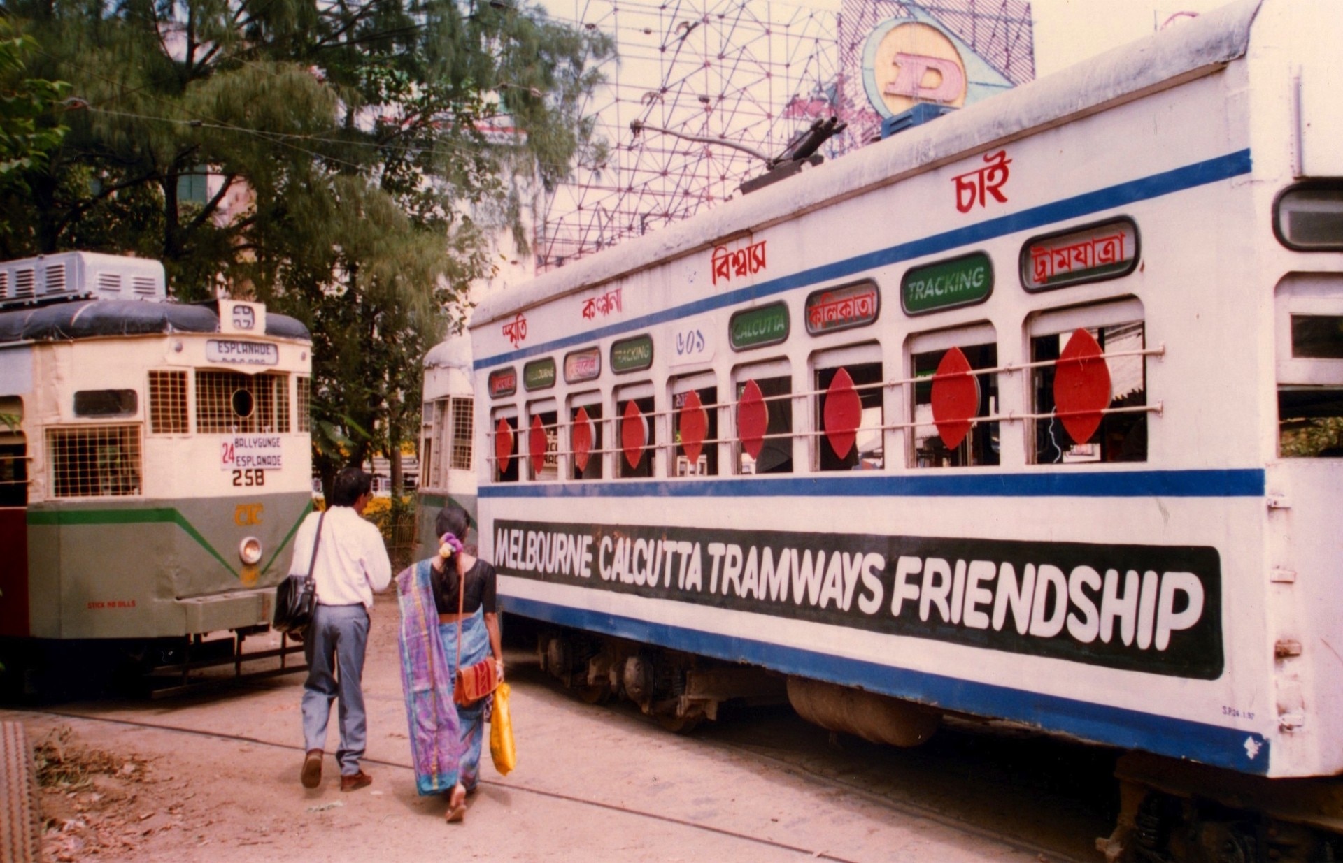 Un hombre y una mujer caminan hacia un tranvía blanco adornado con las palabras 