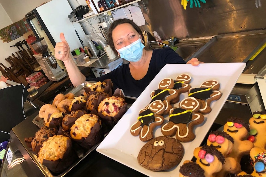Bakery worker Simona holds up a tray of gingerbread men and does the thumbs up.