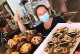 Bakery worker Simona holds up a tray of gingerbread men and does the thumbs up.