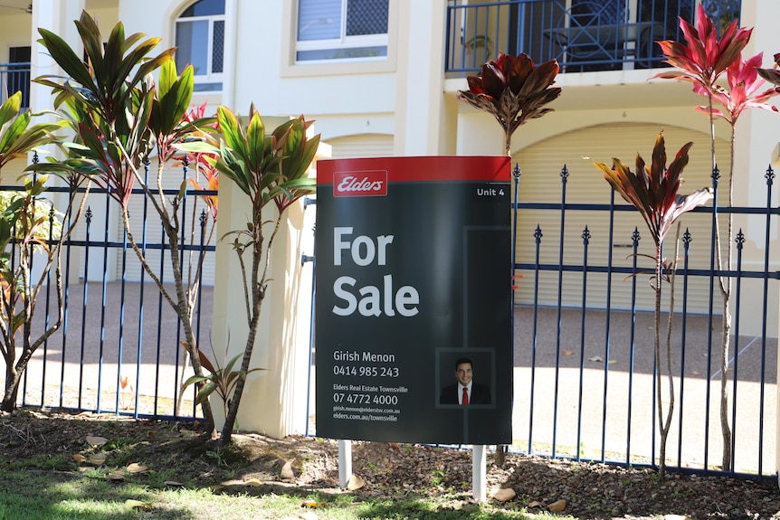 A for sale sign in front of a block of units
