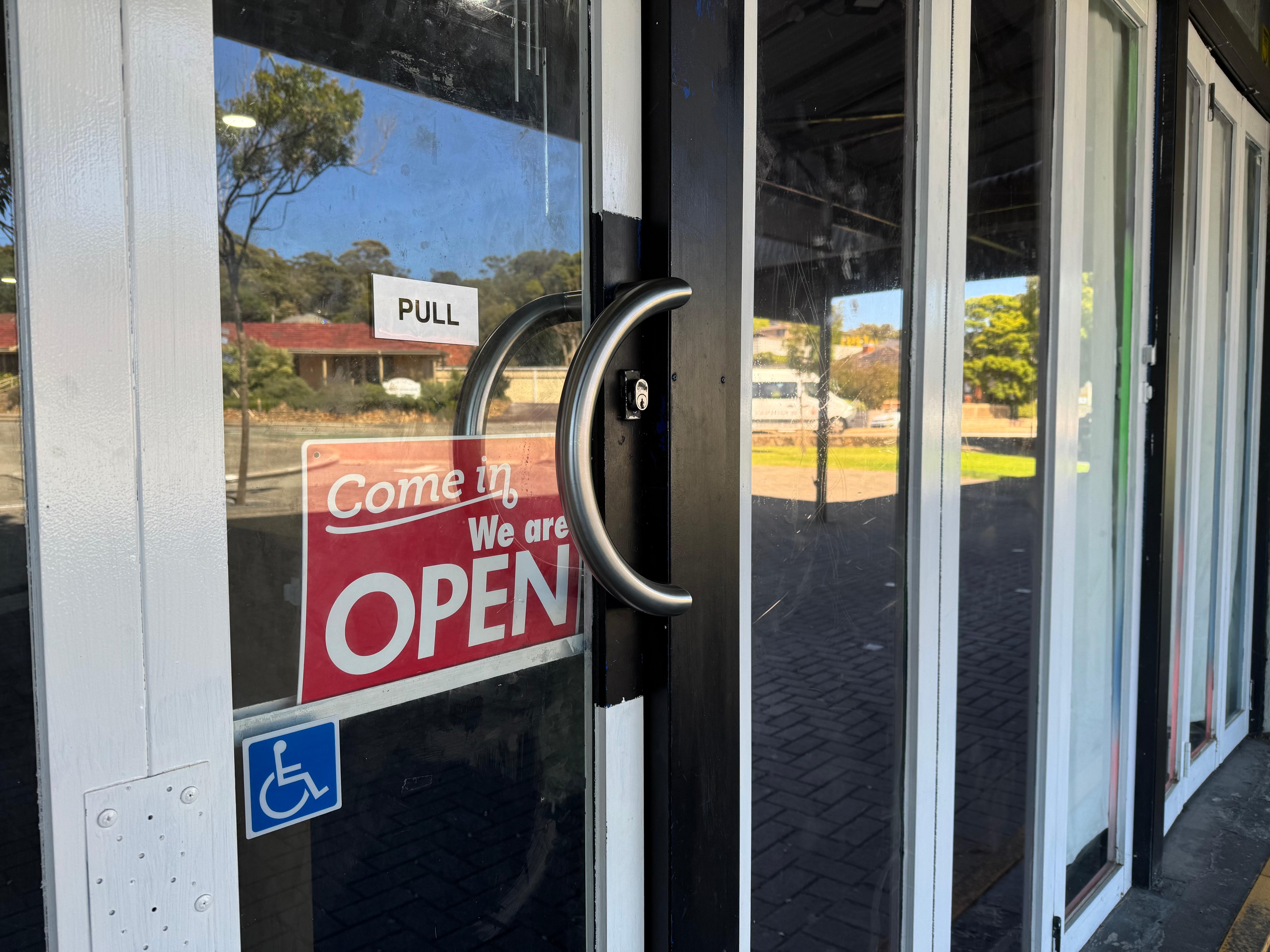 A sign saying 'come in, we are open', hung on a glass store door. 