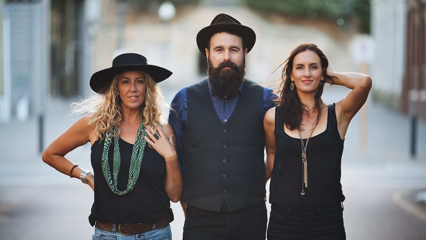 A man and two women stand in an alleyway, smiling.