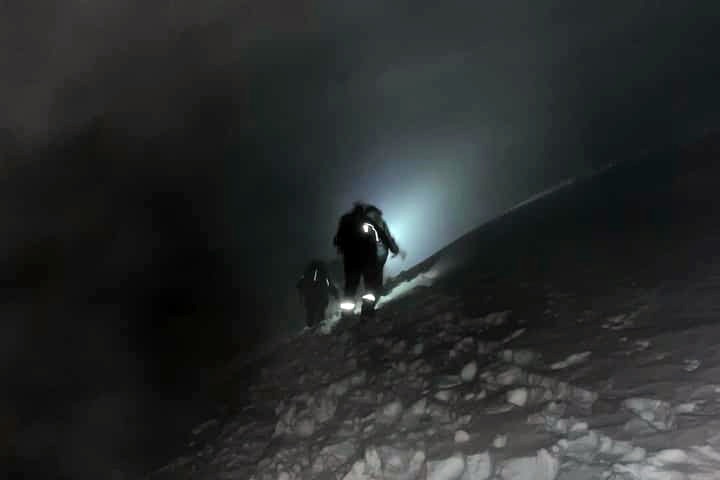 People climb a snowy mountain at night.