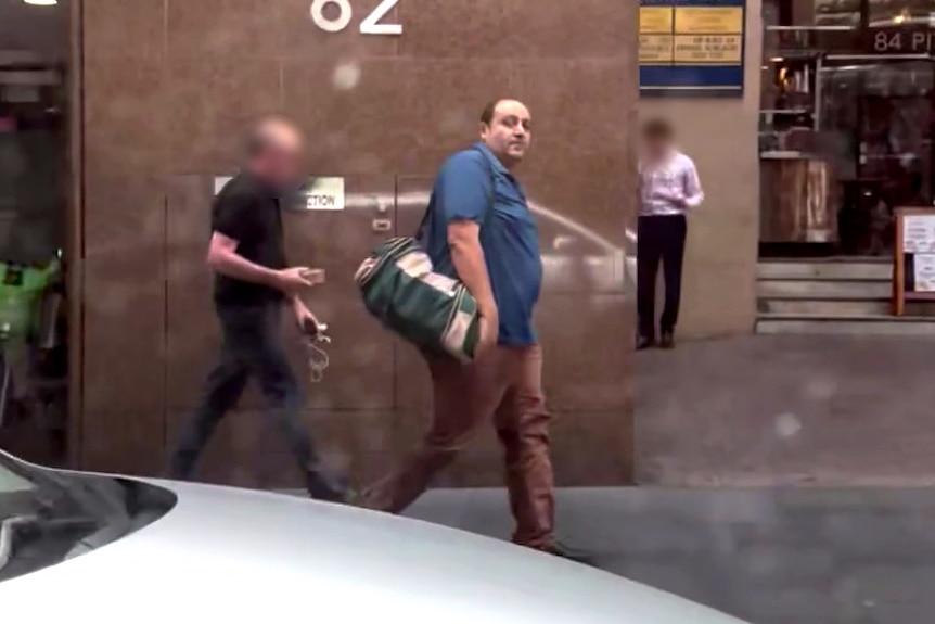 一名中年男子在城中行走时，侧目望去。 他的肩上挎着一个行李袋。