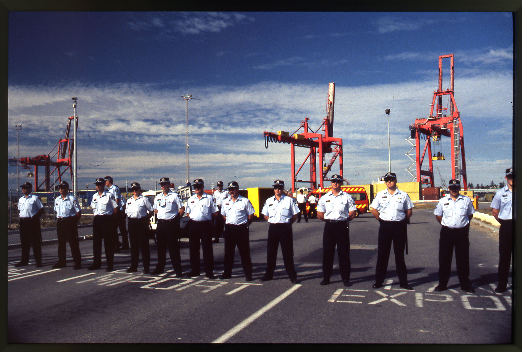 A group of police line up against the background of cranes along the waterfront 