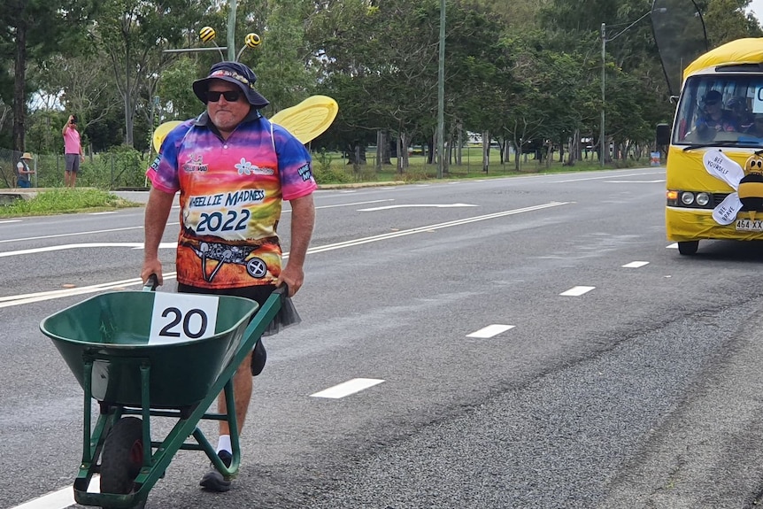 A man in a bee outfit pushing a wheelbarrow along the road