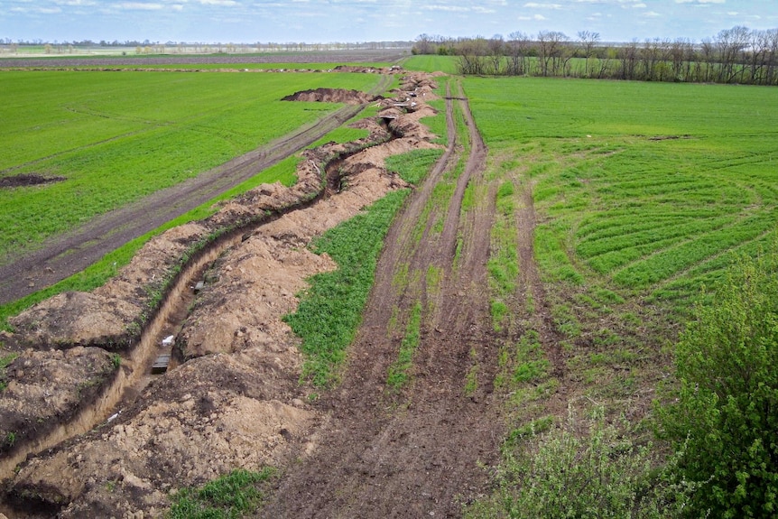 A long trench dug into bright green grass in a field.