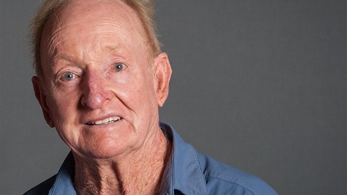 Rod Laver smiles directly at the camera. He is wearing a blue shirt.
