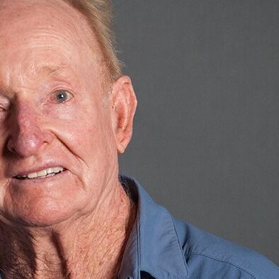 Rod Laver smiles directly at the camera. He is wearing a blue shirt.
