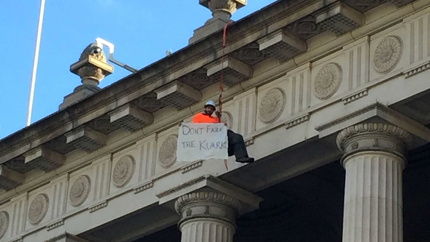 A protester abseiled down the front of the Victorian Parliament building with a sign saying 'Don't fark the Kuark.'