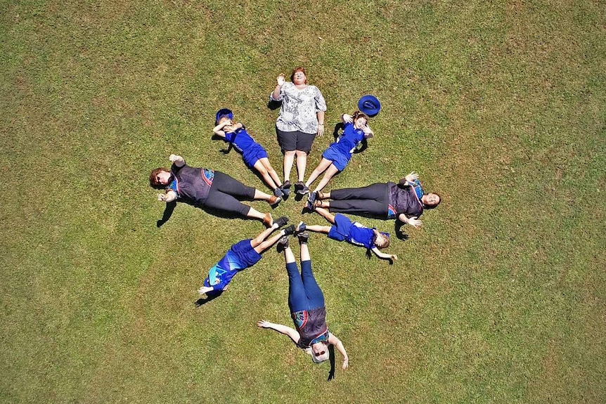 The students and staff of Abergowrie State School lie on the school oval with their feet touching in a circle chape