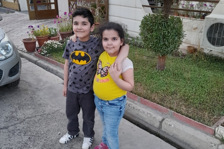 Refugee children George and Elinor Al Daoud standing with arms around each other in an Erbil street.  