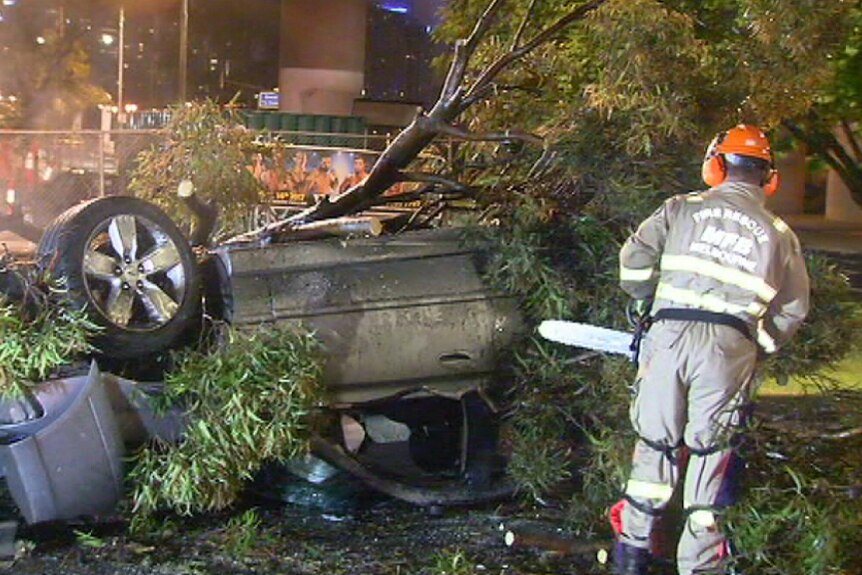 Emergency crews use chainsaws to access a car that flipped onto its roof and hit a tree.