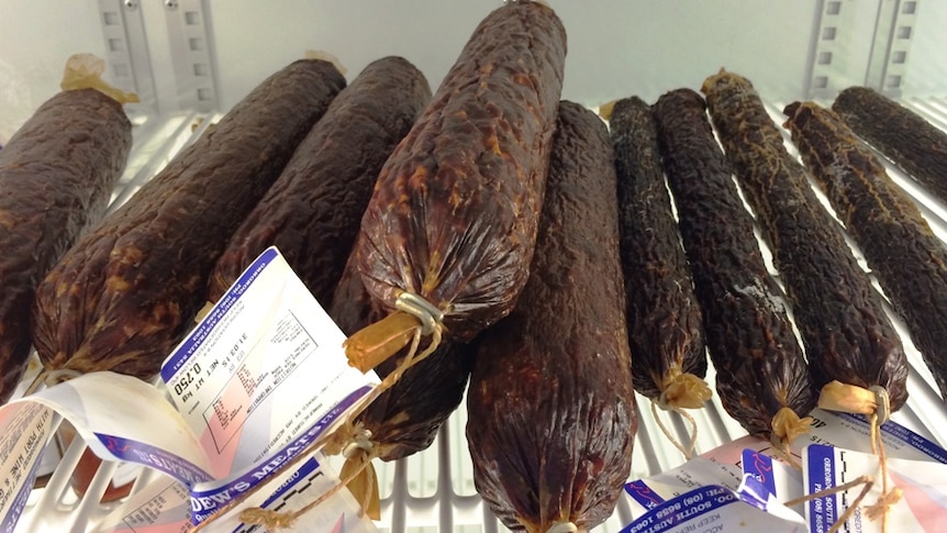 A pile of salami sticks in a meat cabinet.