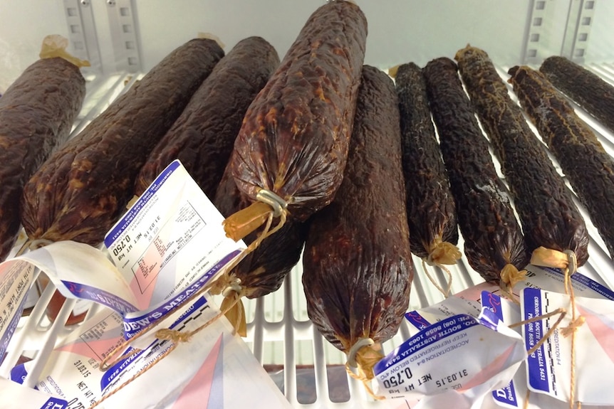 A pile of salami sticks in a meat cabinet.