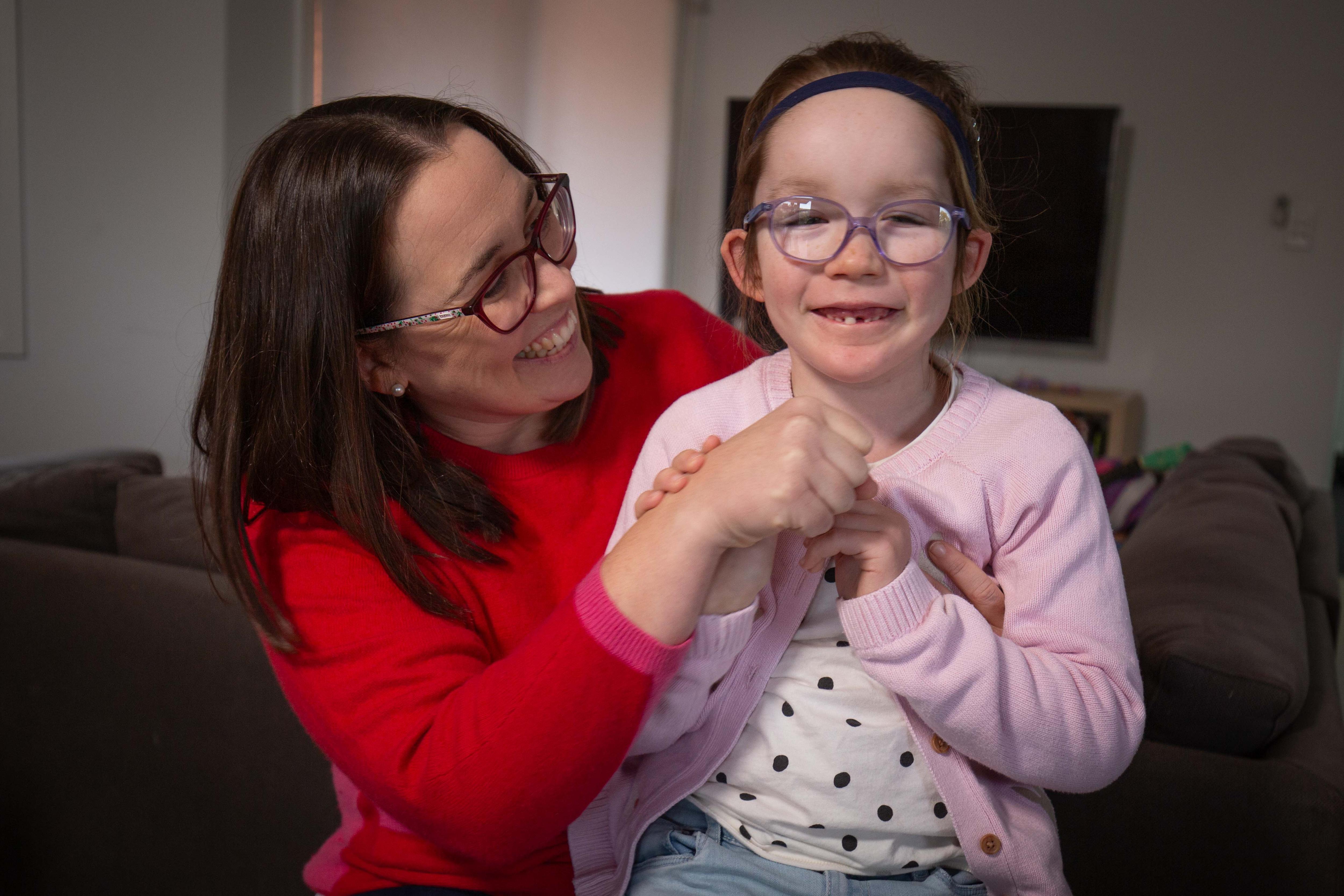 A smiling woman sits with her laughing daughter on her lap.