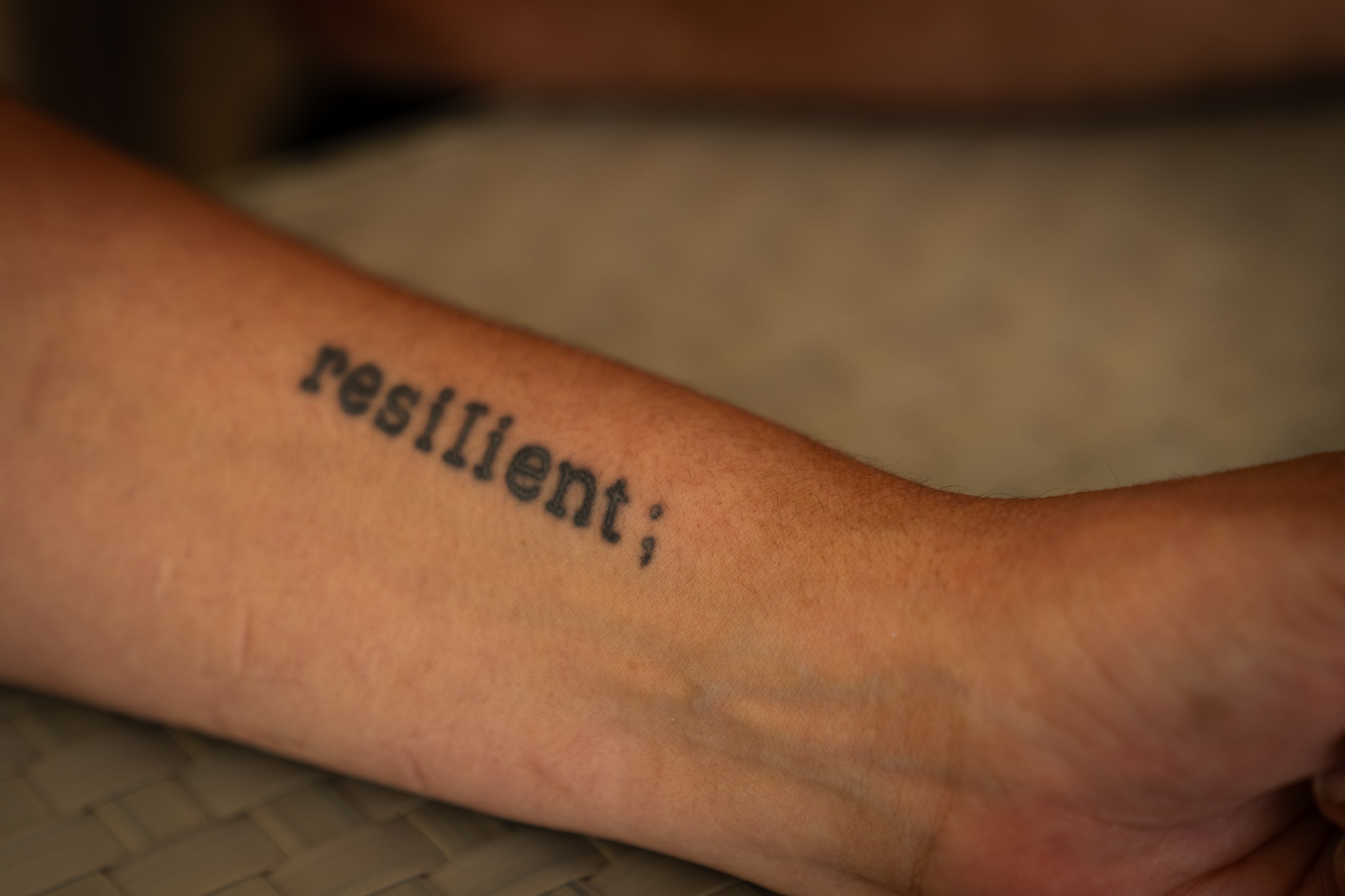 A womans for arm with a short 15cm tattoo in text reading resilient in lower case with a semi colon at the end, the tatto