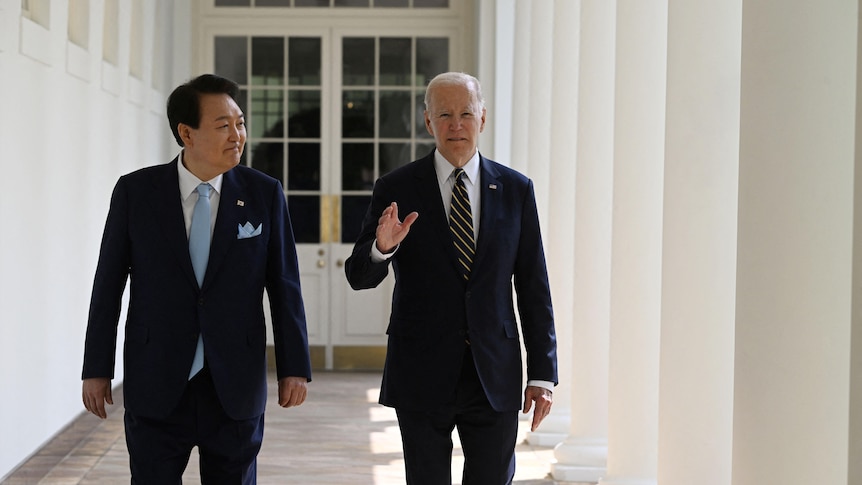 Mr Biden and Mr Yoon are in suits while walking through the colonnade of the White House.