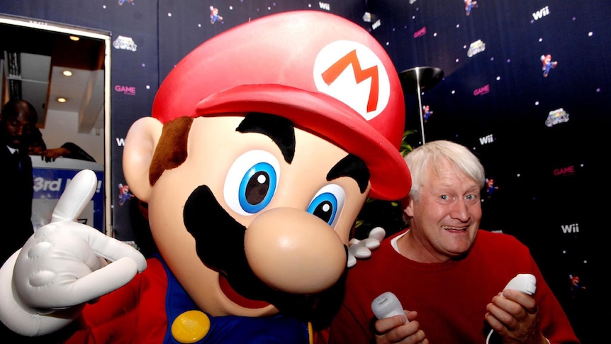 An olde man posing with an oversized Mario figure.