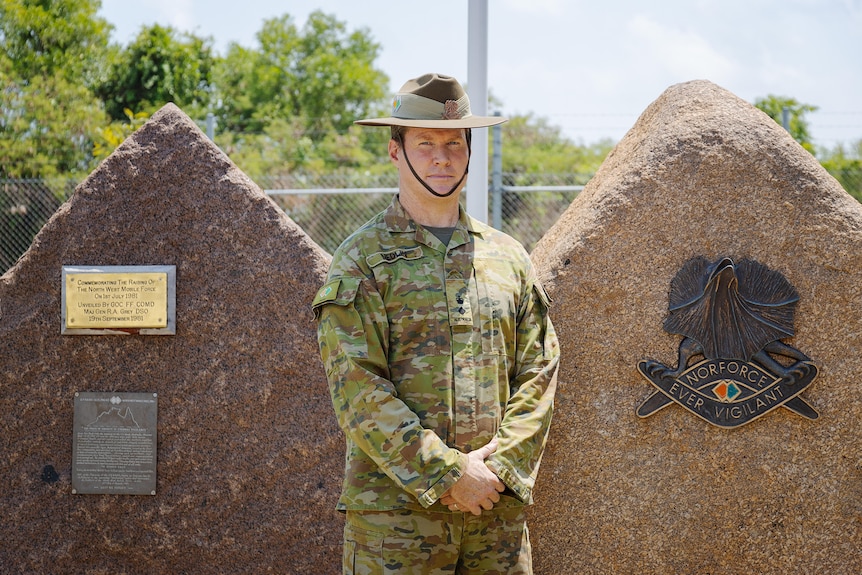 a man wearing australian army uniform in front of two rocks with plaques on them