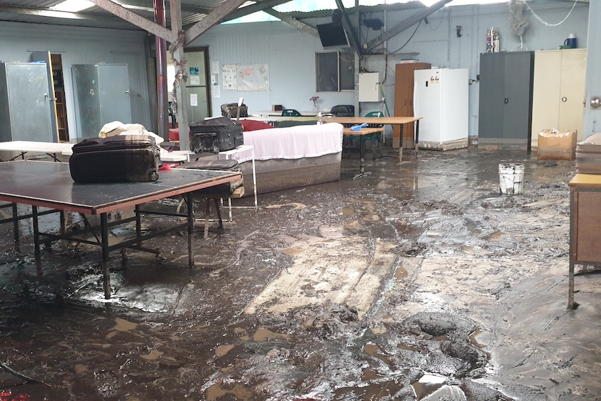 a common room in a workers' accommodation building is flooded with ankle-deep mud. Personal items are up on tabletops