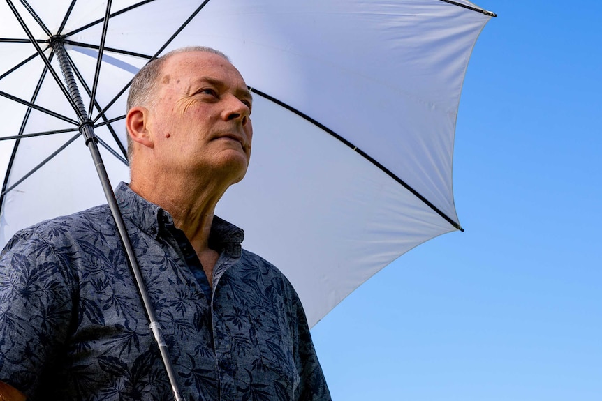 Bruce Buckley, a meteorologist, carrying an umbrella looking into the distance.