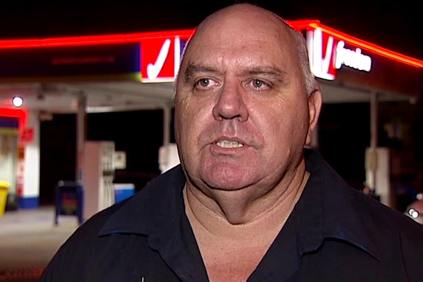 A man standing outside a petrol station at night