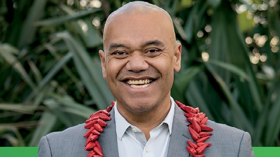 Man smiles to camera in grey suit and red ula around his neck.