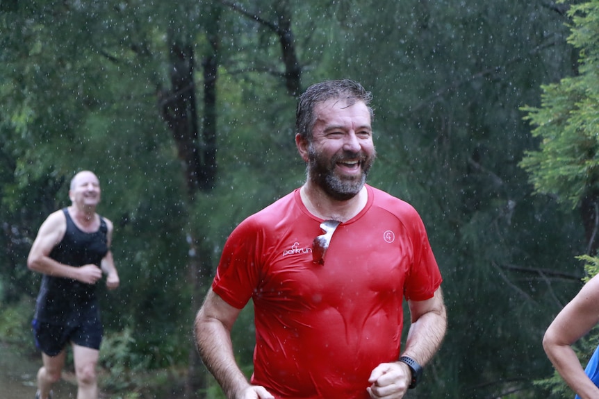 A man laughs while running in the rain at parkrun.
