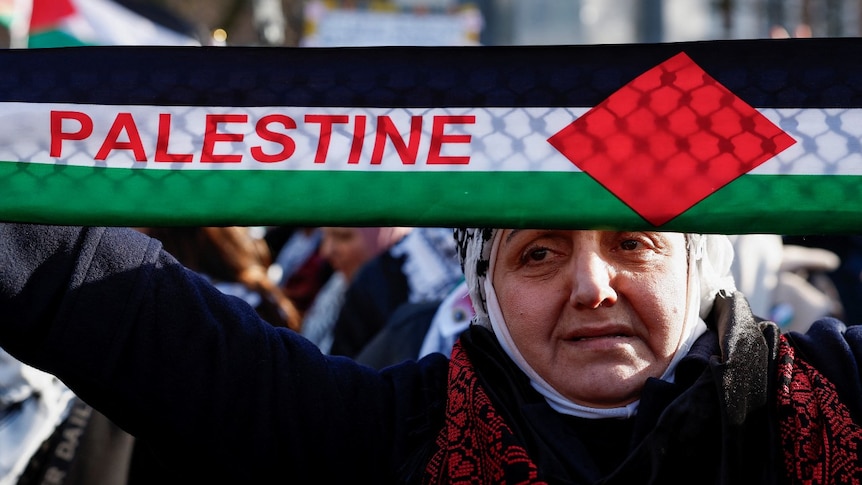 A woman holding a scarf that says Palestine on it
