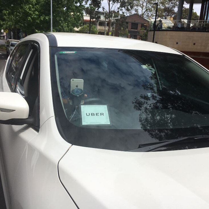 An Uber identification sticker on the windscreen of a white sedan.