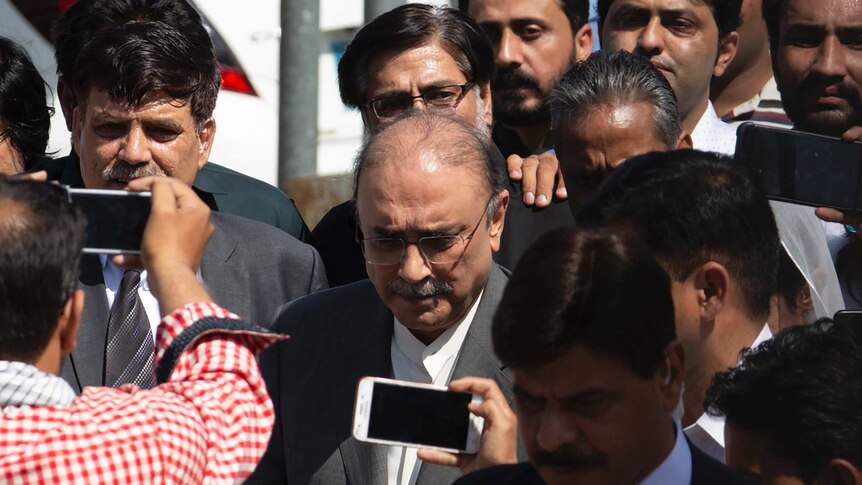 Asif Ali Zardari wears a suit and is surrounded by dozens of people as he leaves court