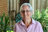 old woman in a pink shirt standing in front of green plants 