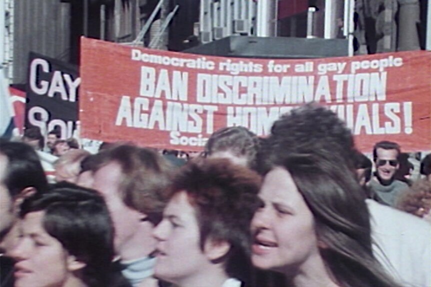 people rally through sydney streets in the 80s carrying a banner that reads ban discrimination against homosexuals