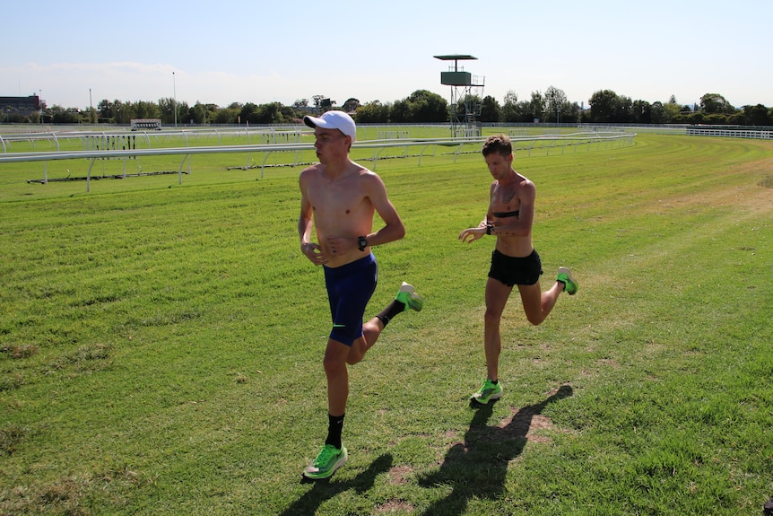 Stewart McSweyn runs with a teammate on grass at a racetrack