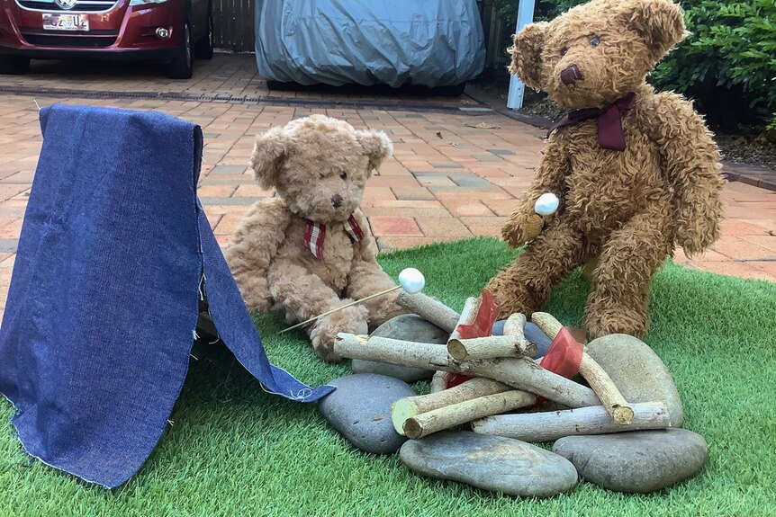 Two teddy bears sit in a driveway near a fake camp fire.