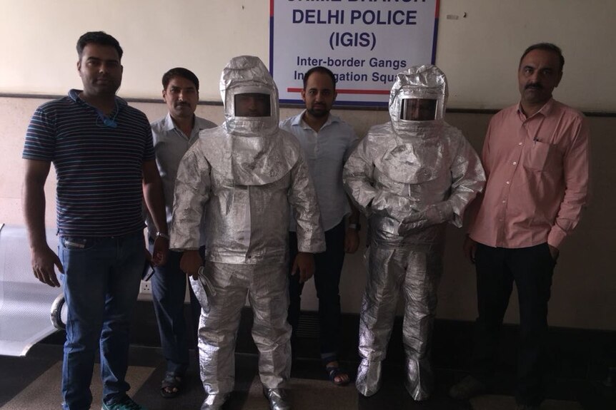 Two men in chemical suits stand with police at a New Delhi Police Station