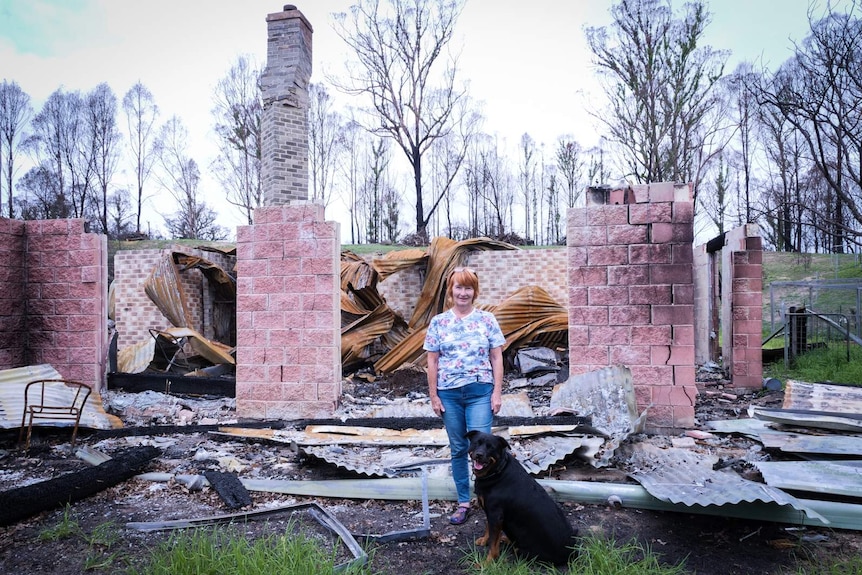 A woman stands amid the ruins of a home with pink brink walls and sheets of corrugated iron on the ground.