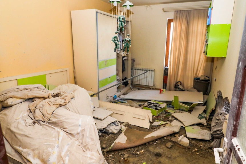 The wall of a bedroom is blown in and debris is spread across the floor after a shelling attack
