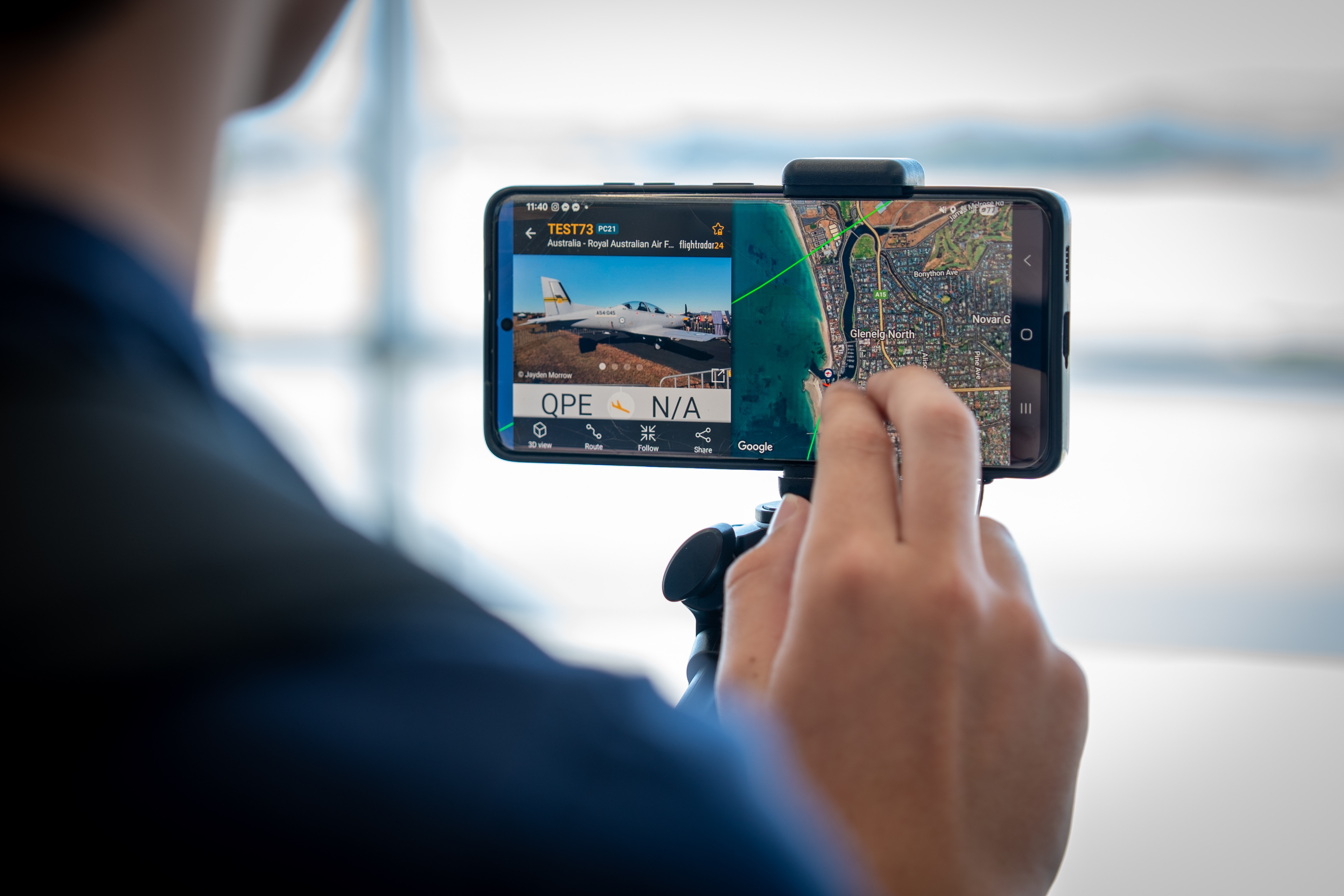 Dedo sosteniendo un teléfono inteligente que muestra un mapa y una imagen de un avión