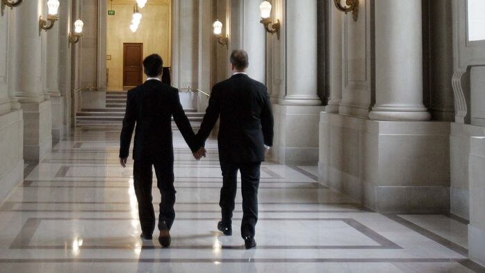A gay couple walk down a hallway