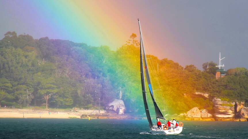 A yacht appears to sail into one end of a rainbow on Sydney Harbour.