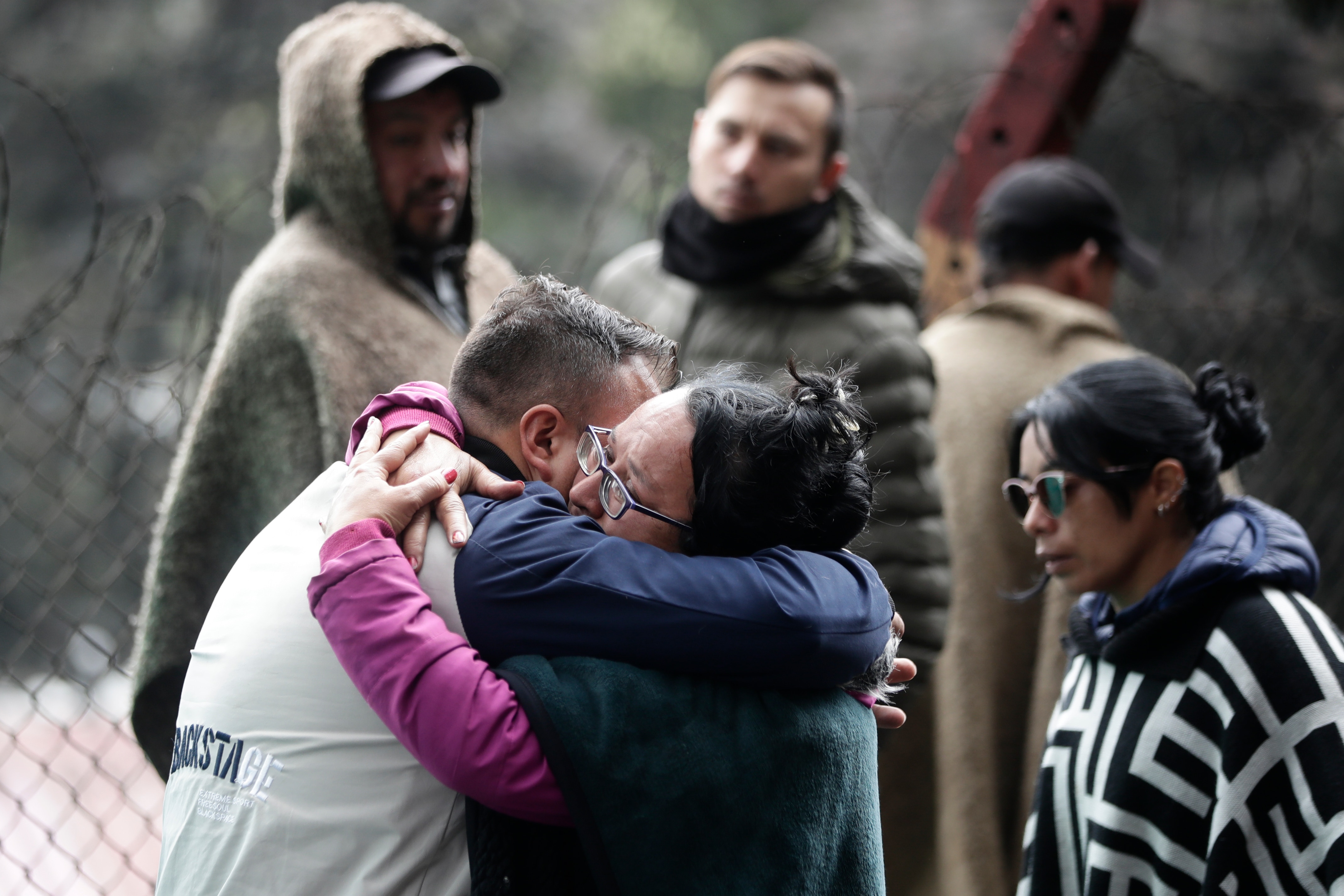 Two people hug next to a barbed wire fence as three others watch on. 