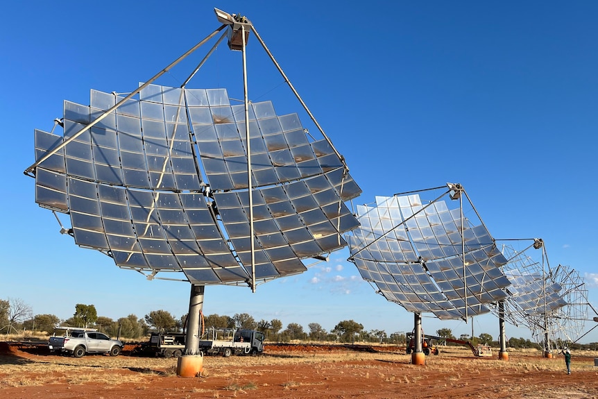 Solar dishes in a line. Truck and car in the background.