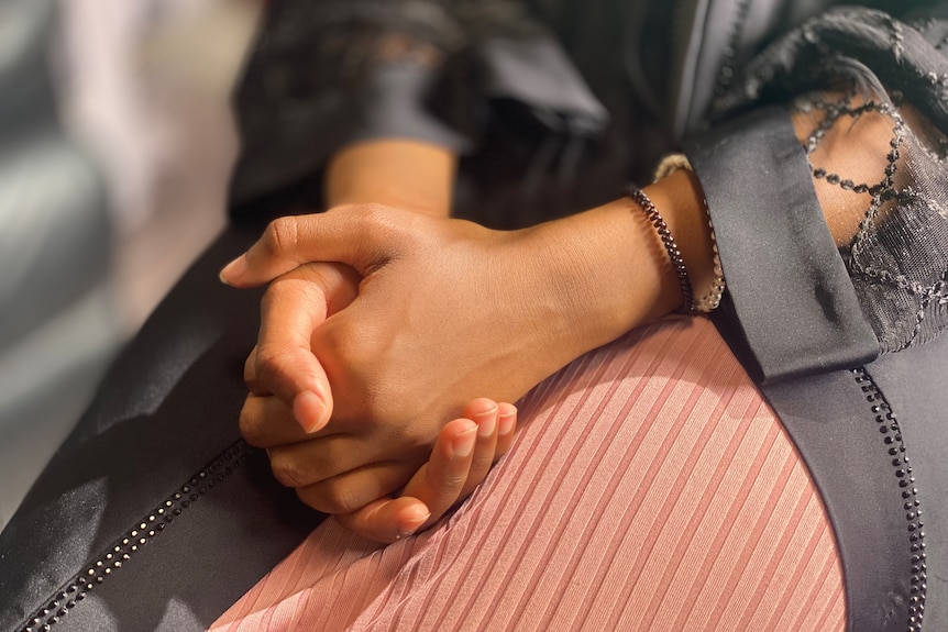 The hands of a young teenage girl, folded in her lap.
