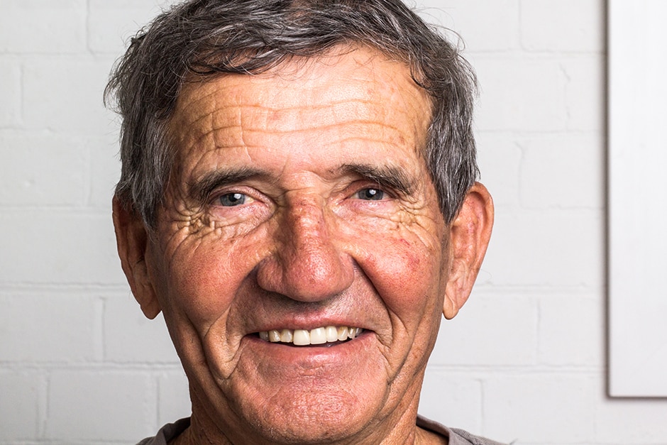 An older man in front of a white wall.